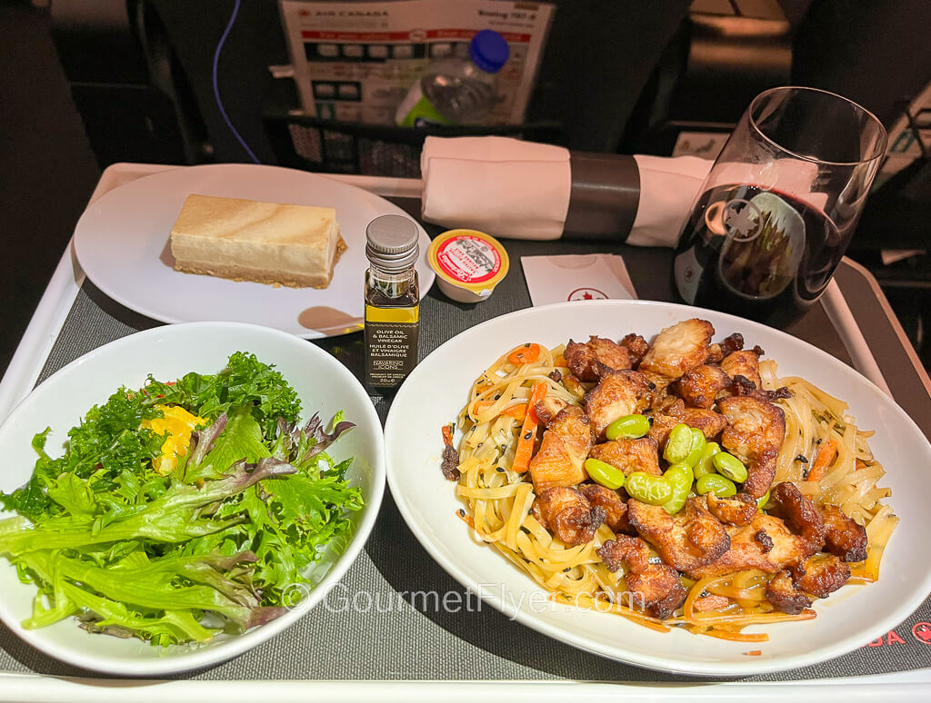 Review of Air Canada's Premium Economy features a dinner tray with a plate of chicken meat, a green salad, and dessert.