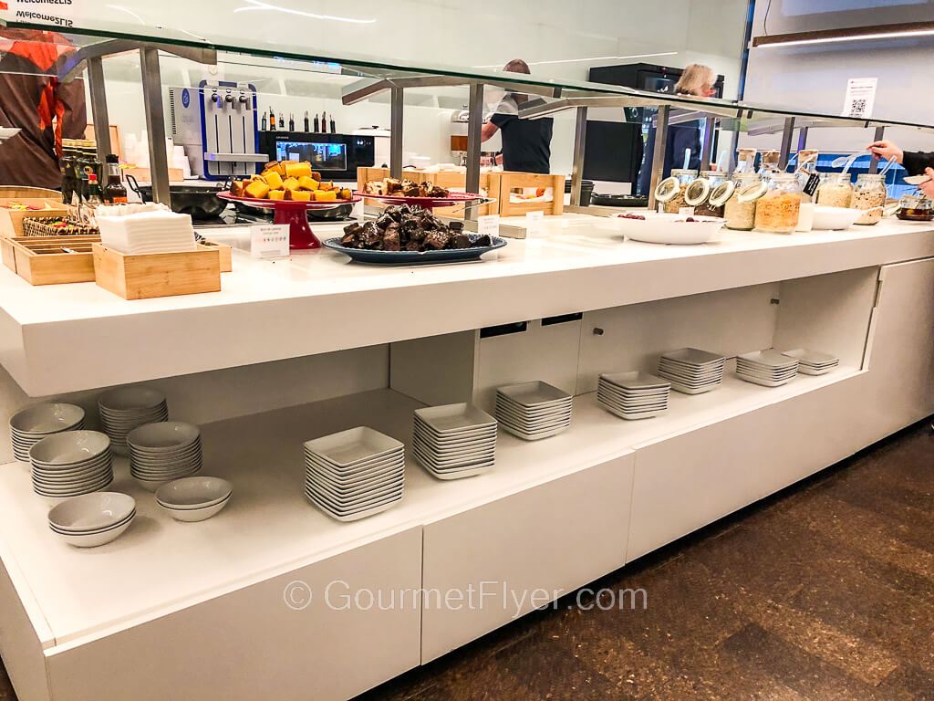 A long buffet counter is completely filled with food, including jars of cereals on the right and baked goods on the left.
