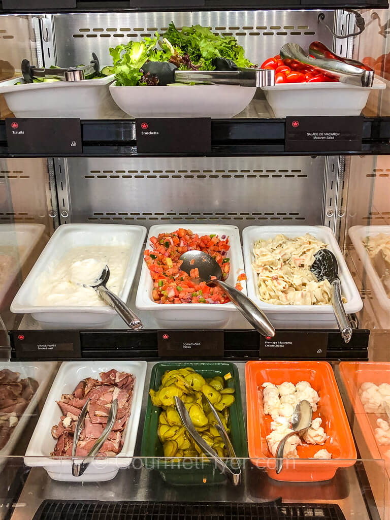A tall open refrigerated space holds trays of vegetables and meats.
