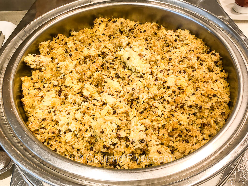 A large round silver container is filled with white rice that is topped with sprinkles of brown lentil bens.