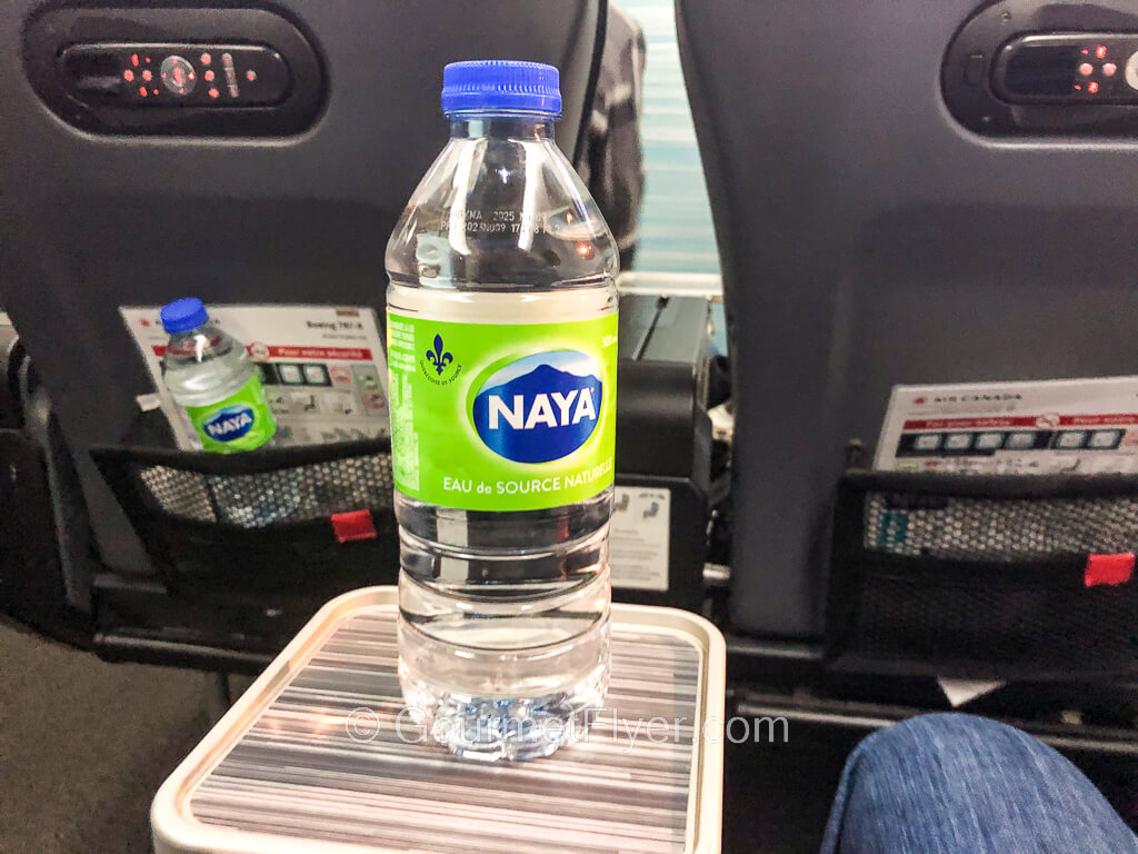 A bottle of Naya brand water is standing on the beverage tray of the armrest of an airplane seat.