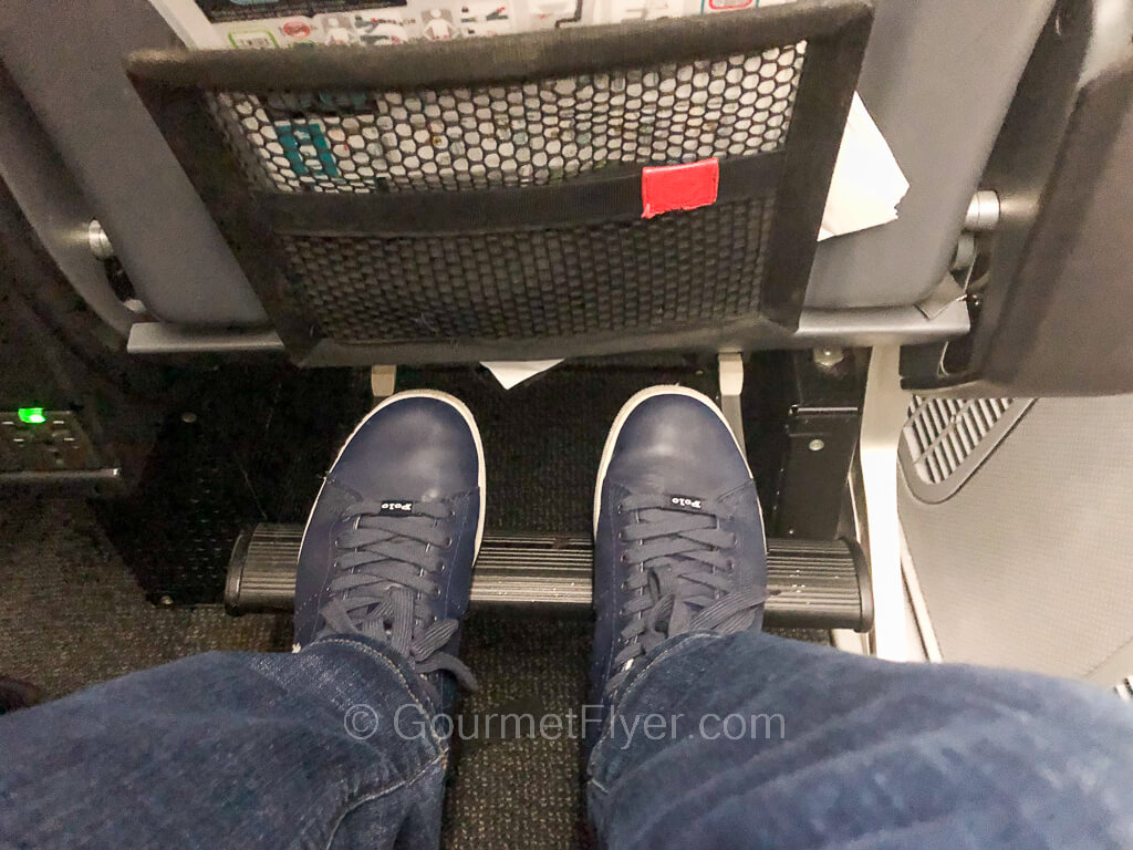 A passenger places his feet on the footrest of an airplane seat.