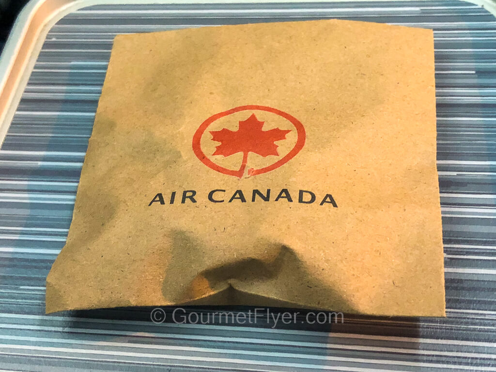 A brown square envelope with Air Canada's maple leaf logo sits on top of a tray table.