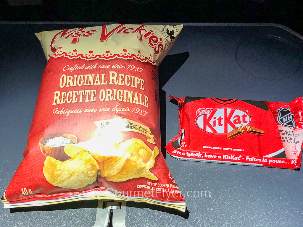 A bag of potato chips and a packet of Kit Kat are placed on a tray table.