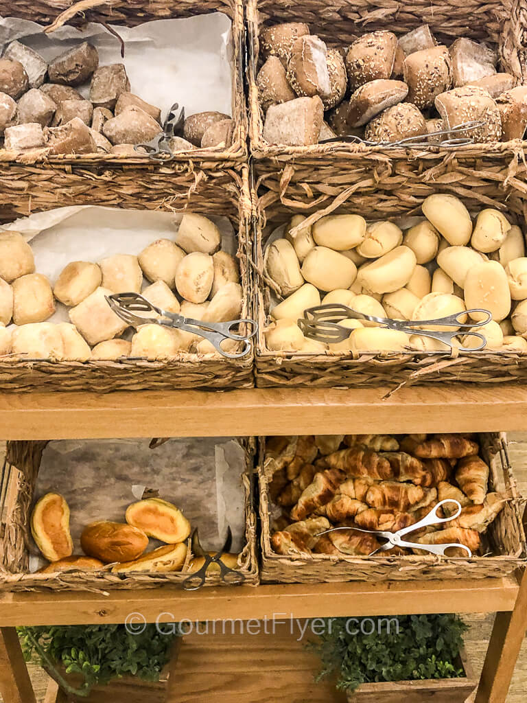 Six baskets stacked on a shelf are filled with different kinds of breads and rolls.