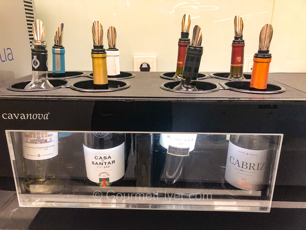 Eight bottles of wine with spout pourers are placed in a compartment with a glass display.