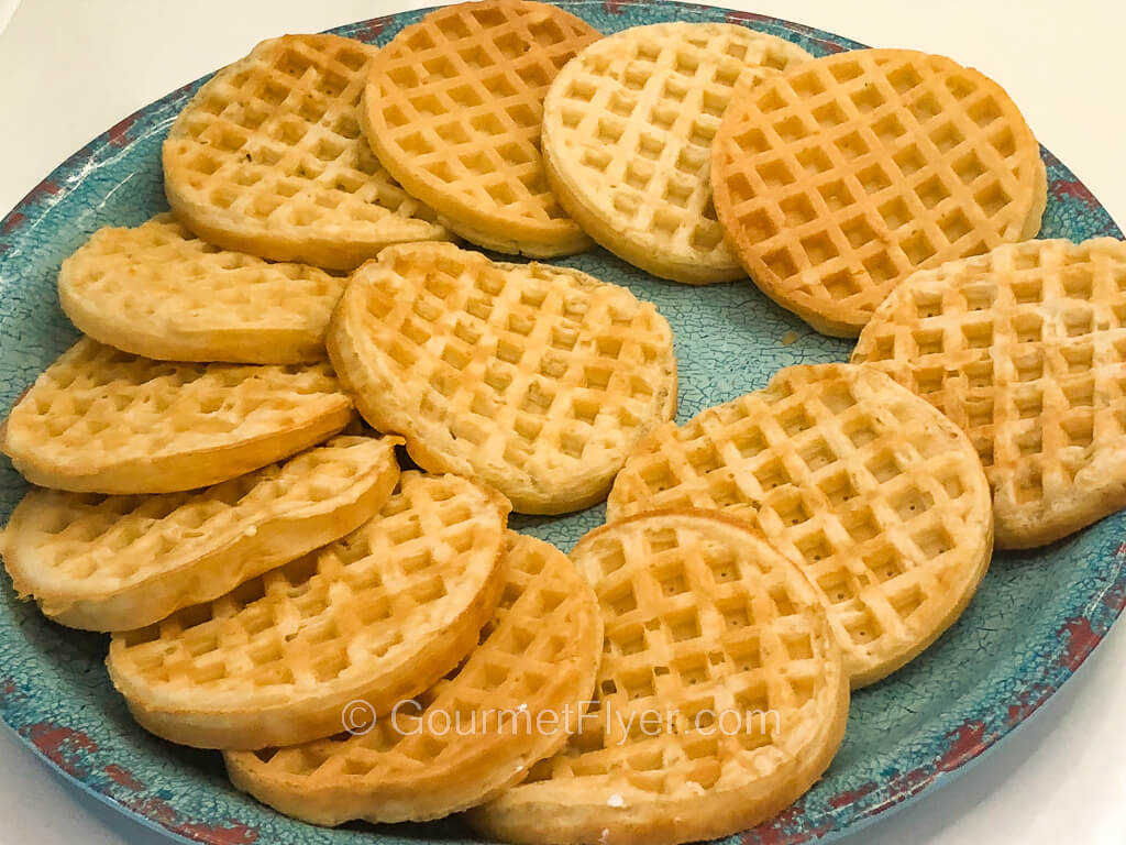 A green serving plate has many waffles placed on it arranged in a circular pattern.