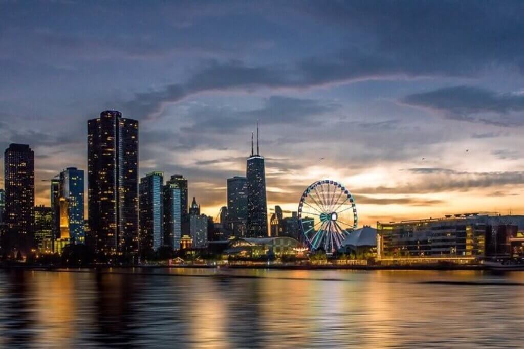 The sun setting over the skyline of Chicago with Sears Tower in the background is accompanied by the Ferris Wheel on the waterfront.