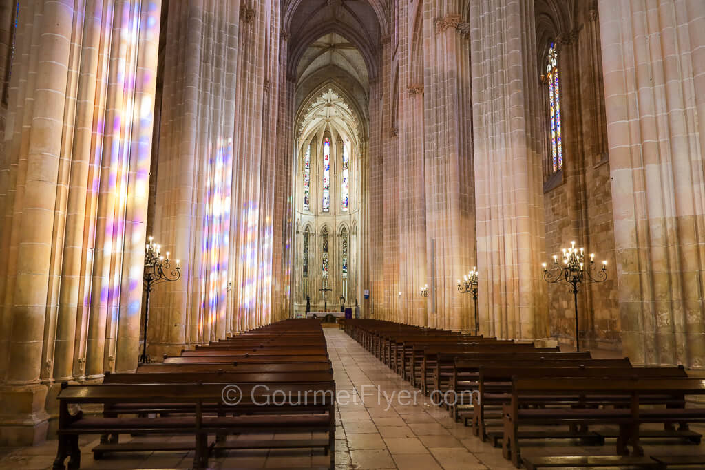 The interior of a church with colorful lights shining on its tall, white, majestic pillars.
