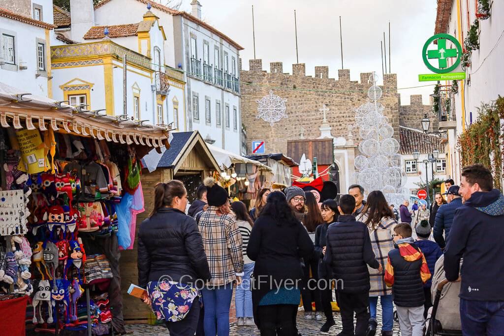 Vendors with merchandise and tourists pack a narrow street with a castle in the background.