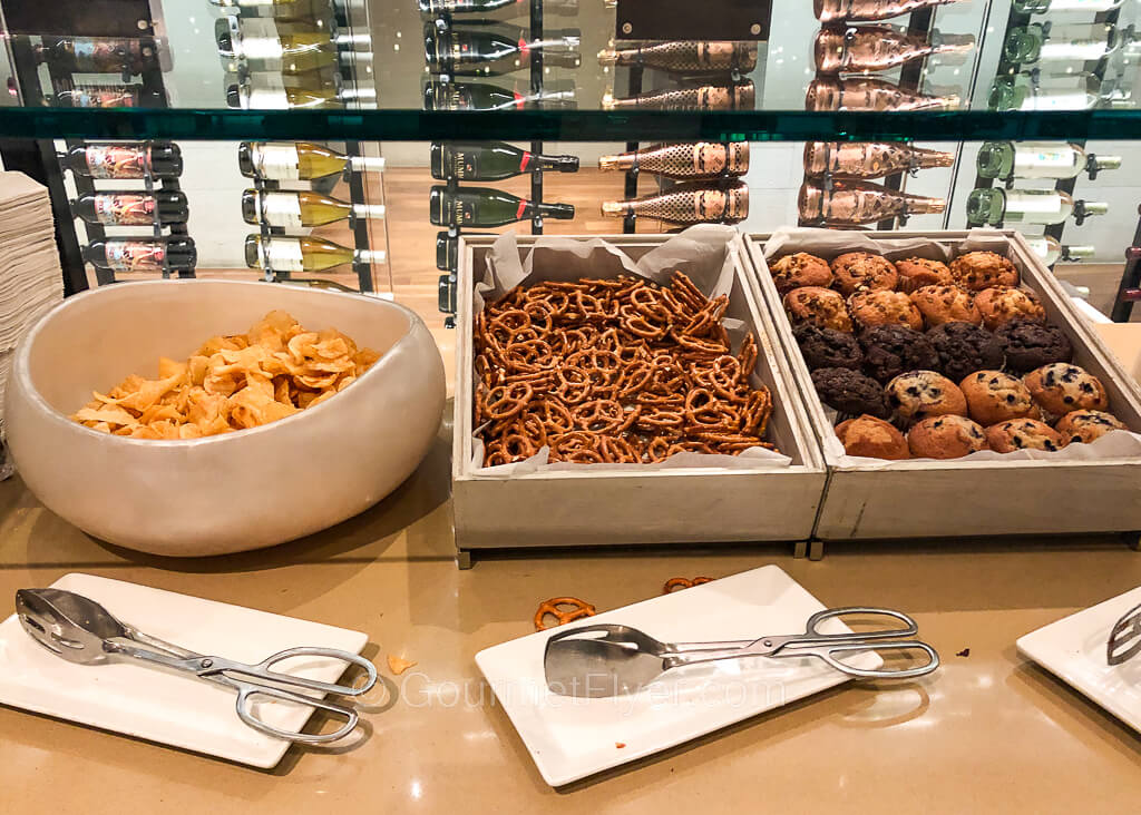 Potato chips, pretzels, and muffins are placed in containers on a countertop.