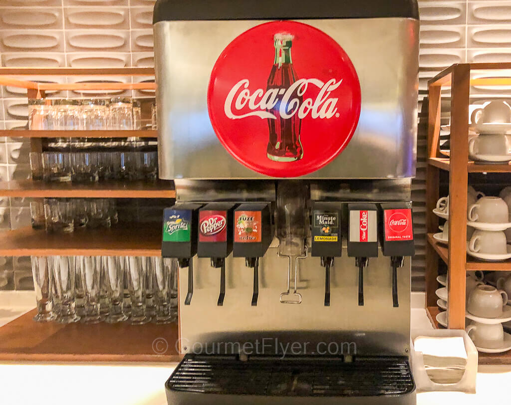 A soft drink machine with a large red Coca Cola logo has 6 dispensers for different drinks.