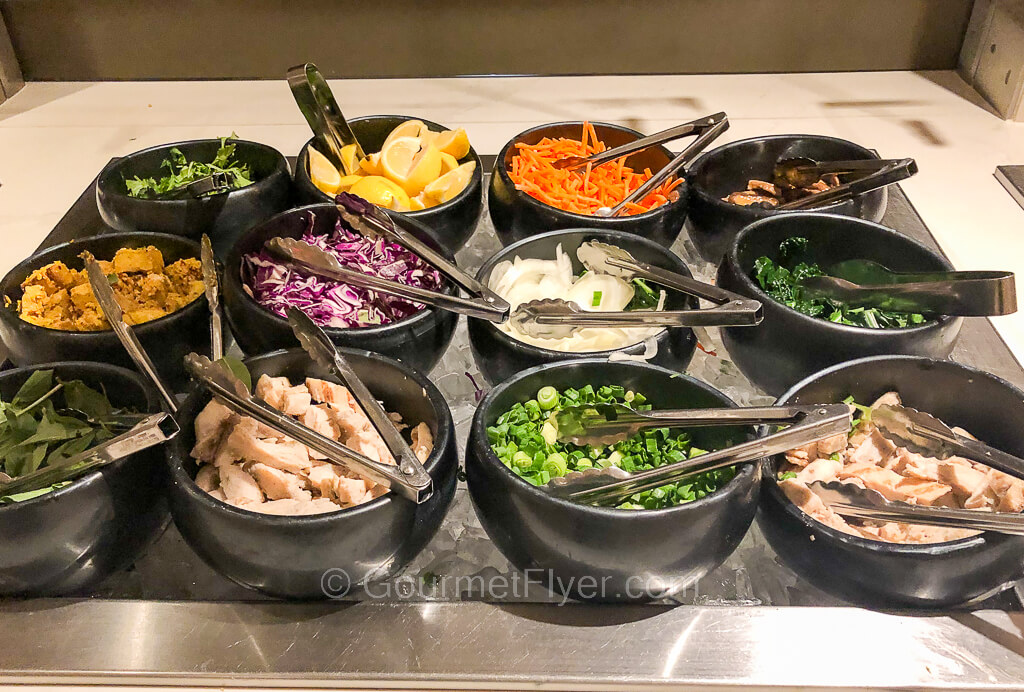 A total of 12 small bowls line up 4 in a row contains a variety of meat and vegetables for soup noodle toppings.