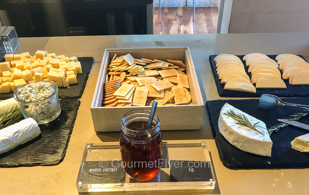 A variety of cheeses are placed on cheeseboards on both sides of a counter with a tray of crackers in the middle.