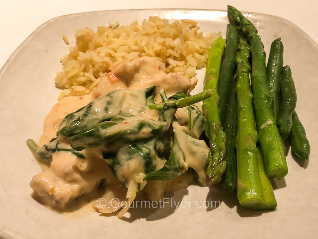 A small plate contains pieces of creamy chicken, spears of asparagus and a small serving of rice.