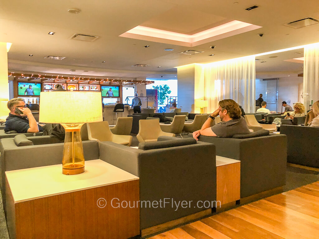 The main lobby area of a lounge has trendy looking sofas with a handful of passengers sharing the space.