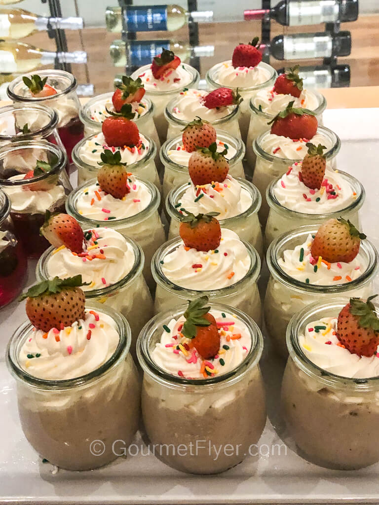 Rows of tall glass containers are filled with a mousse topped with whipped cream and a strawberry.