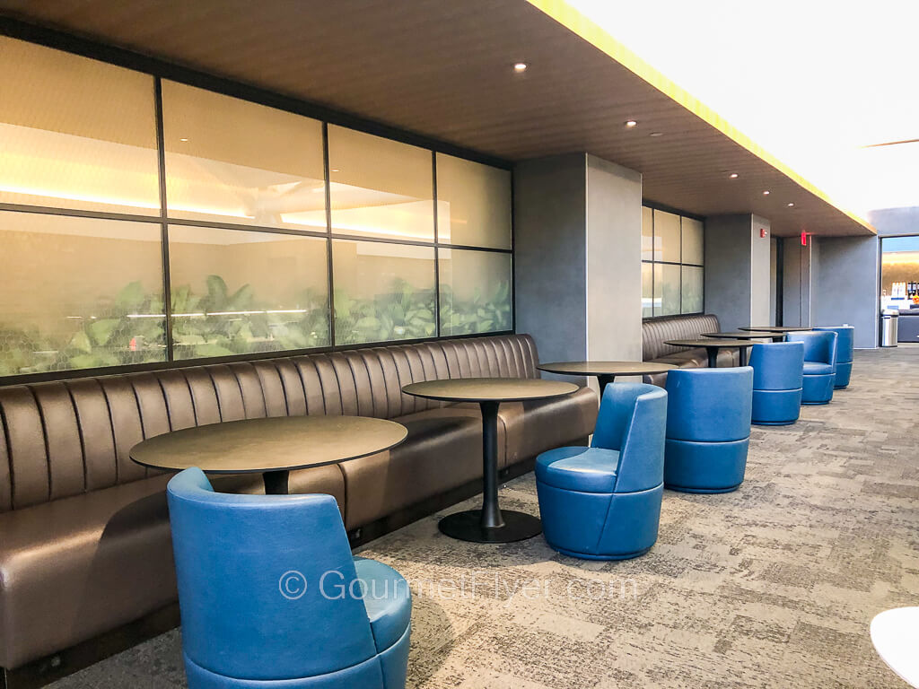 Long sets of sofas line a wall with blue cocktail chairs facing them, separated by a round coffee table.