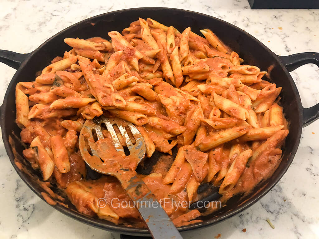 A metal serving platter is filled with penne pasta tossed in a red tomato-based sauce.
