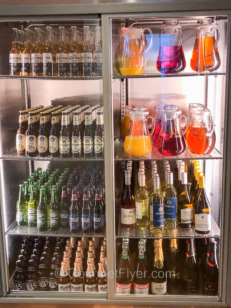 A tall refrigerator with glass stores have 8 compartments each containing a variety of beers, wines, and juices.