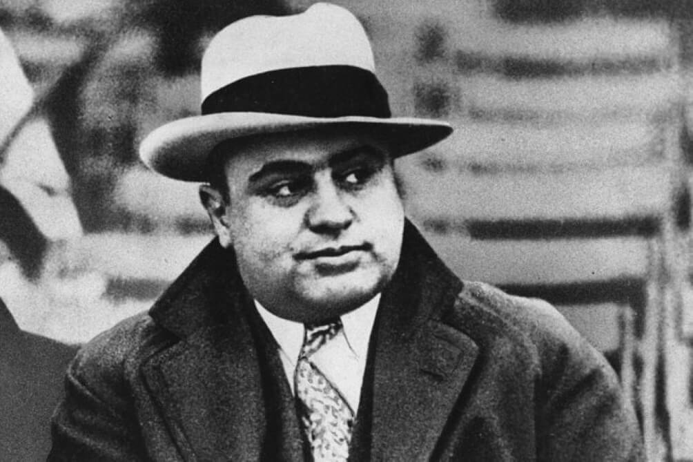 A black and white photo of infamous gangster Al Capone dressed in a suite and wearing a hat.