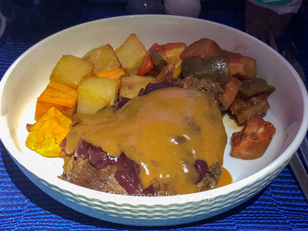 A dish of a slab of meat covered in a brown gravy accompanied with diced potatoes and vegetables.