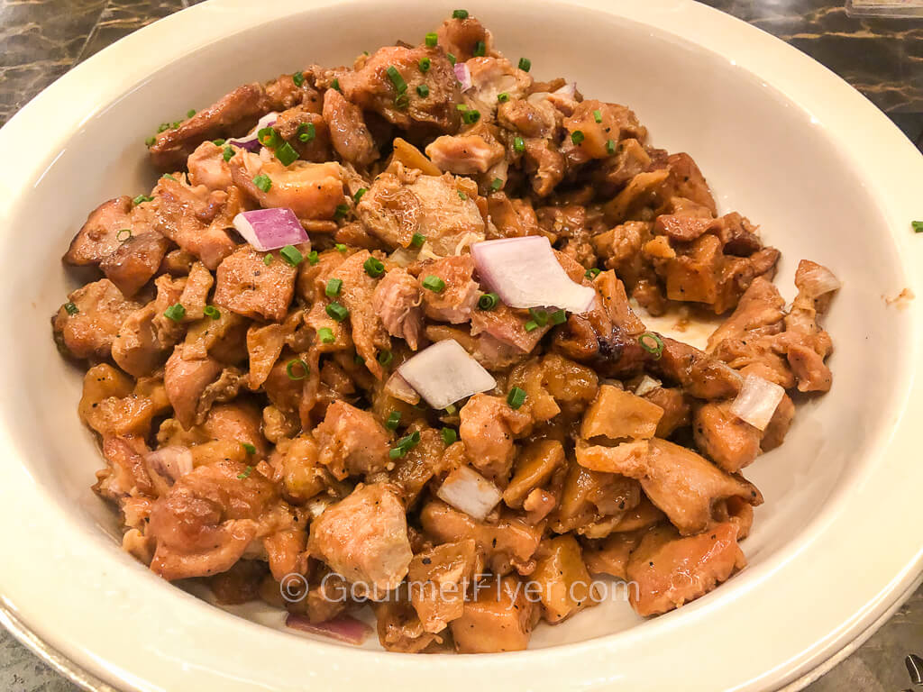 A large serving platter contains sauteed cubed chicken meat garnished with onion and chives.
