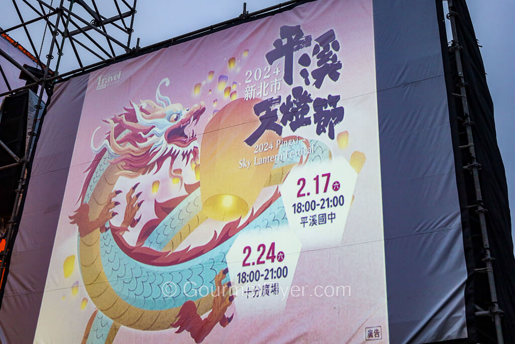 A large screen on stage shows the dates and locations of the Pingxi Sky Lantern Festival with its vibrant dragon graphics.