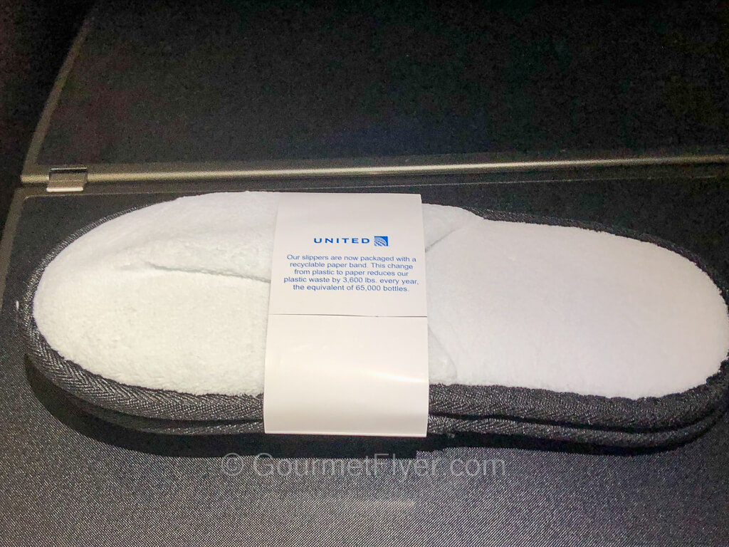 A pair of slippers is held by a paper band with United's logo and is placed on a tray table.