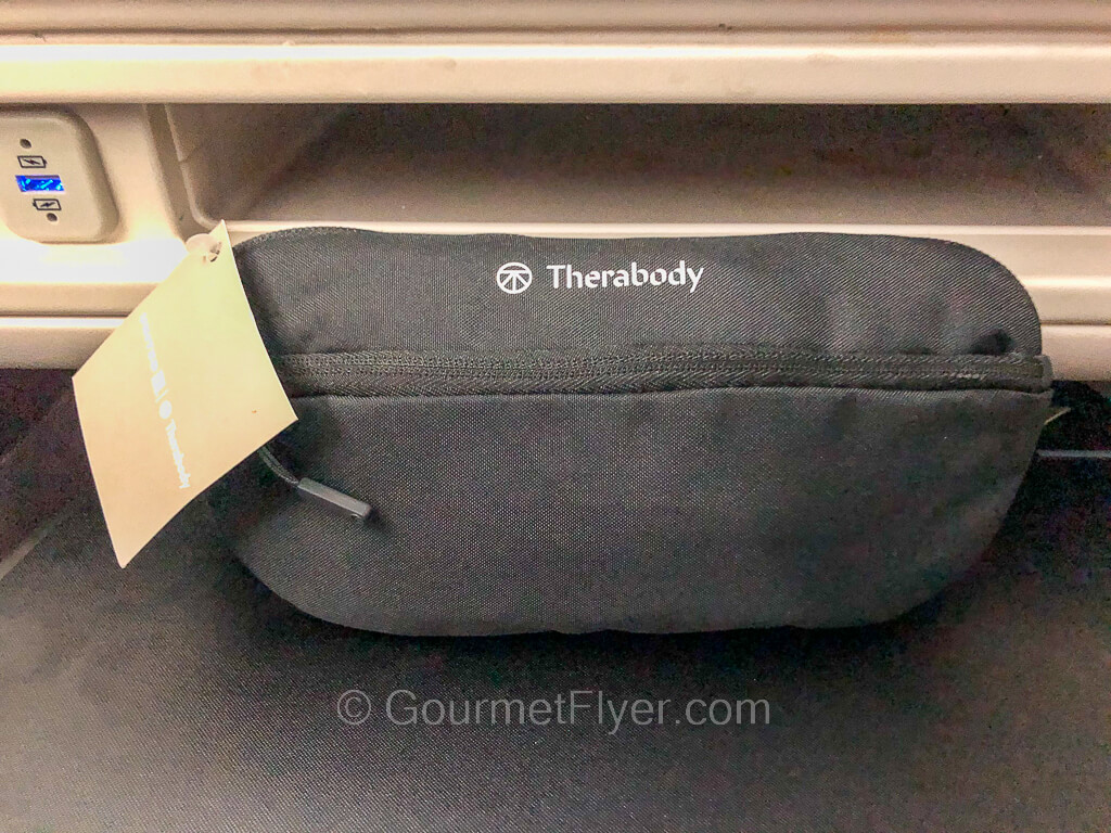A dark gray color fabric pouch is placed on the tray table of an aircraft seat.