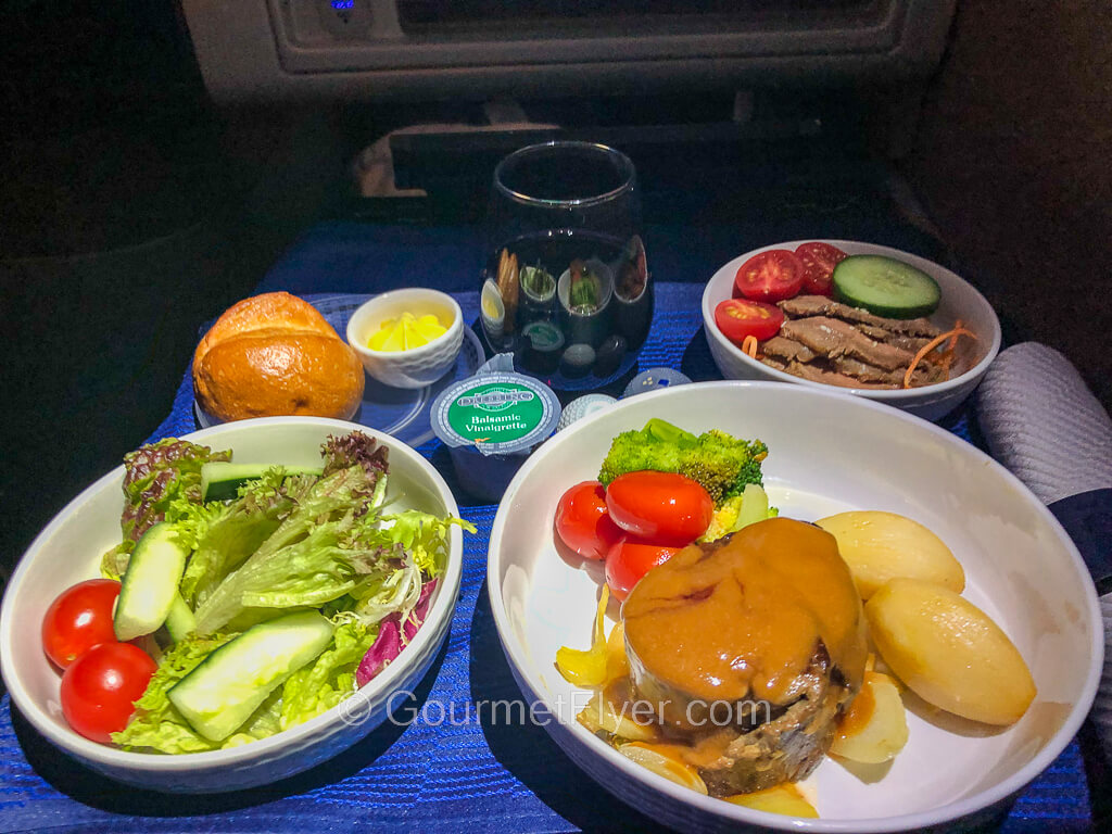 Review of United's Polaris Business Class features a dinner tray with a steak and potato dish accompanied by appetizers, salad, and a glass of red wine.