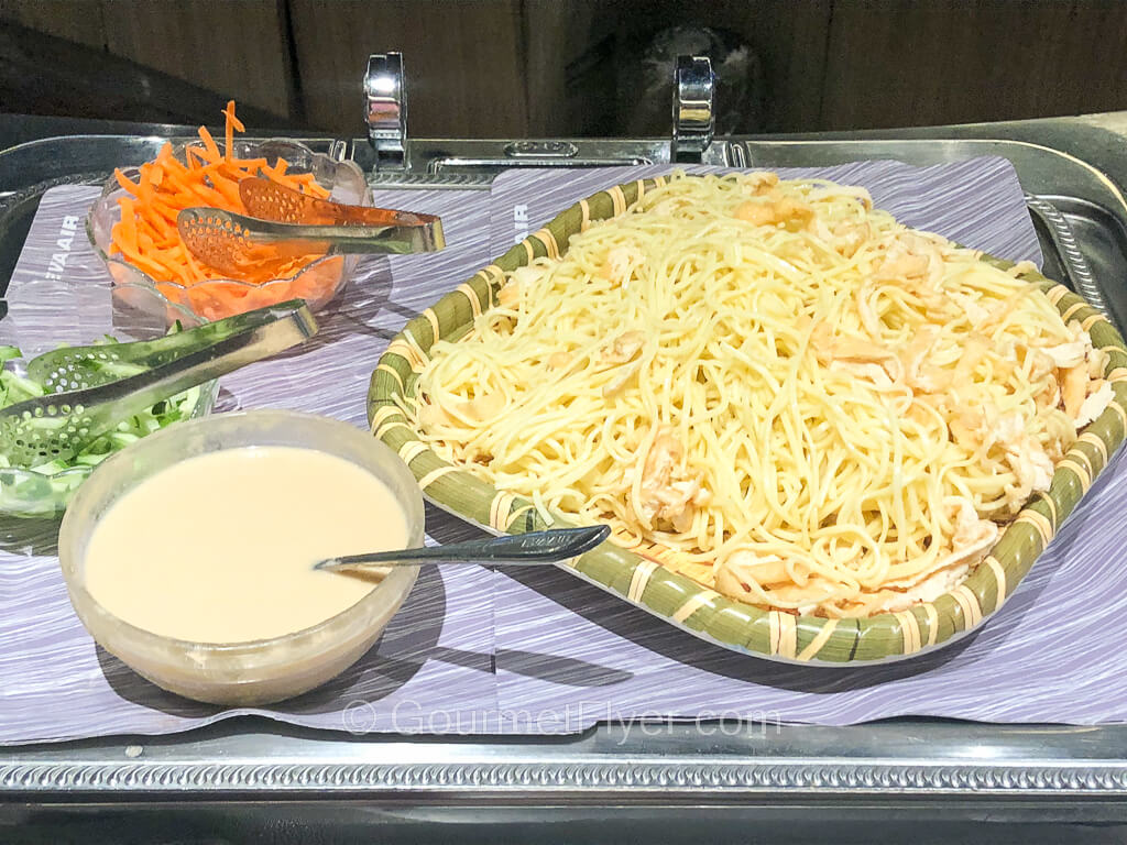 A silver tray contains a large plate of noodles accompanied by a cream sauce and garnishes.