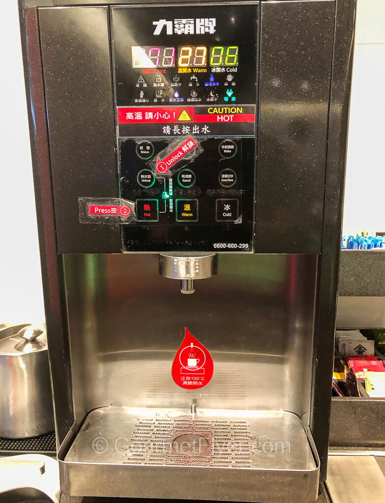 A stainless-steel hot water machine has a digital display and buttons with instructions.