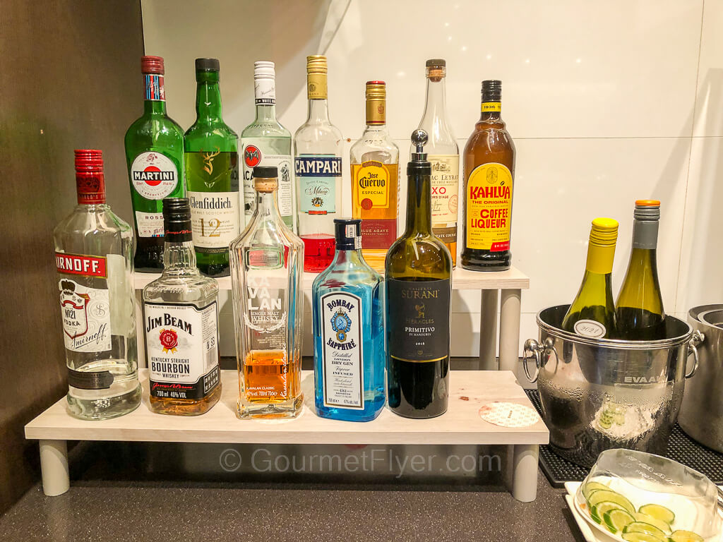 Two rows of bottles of liquors are displayed on a counter. Two bottles of wines are in an ice bucket.
