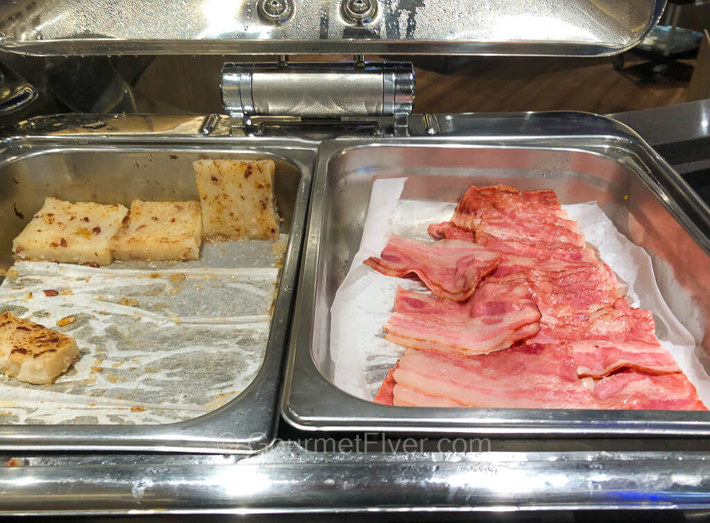 A full tray of bacon is accompanied by only a few pieces of turnip cakes to its left.