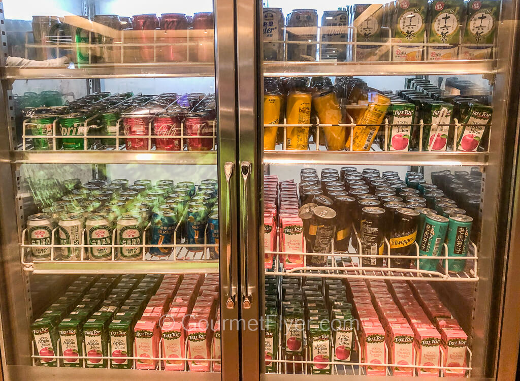 A large refrigerator with double glass doors has a total of 8 shelves carrying a wide variety of soft drinks, juices, and beers.