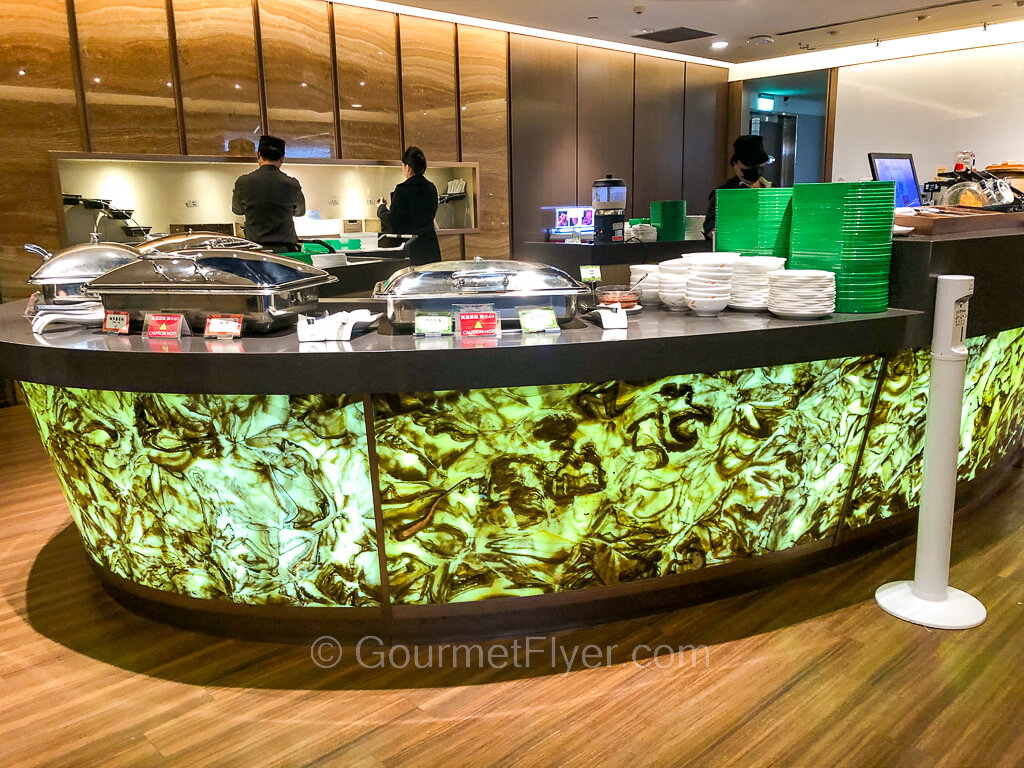 An elegant buffet counter with bright green color graphic has many chaffing dishes and utensils placed on it.