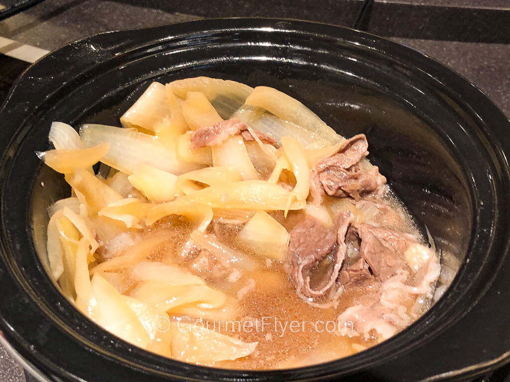 A large bowl contains sliced beef and onions served in a broth.