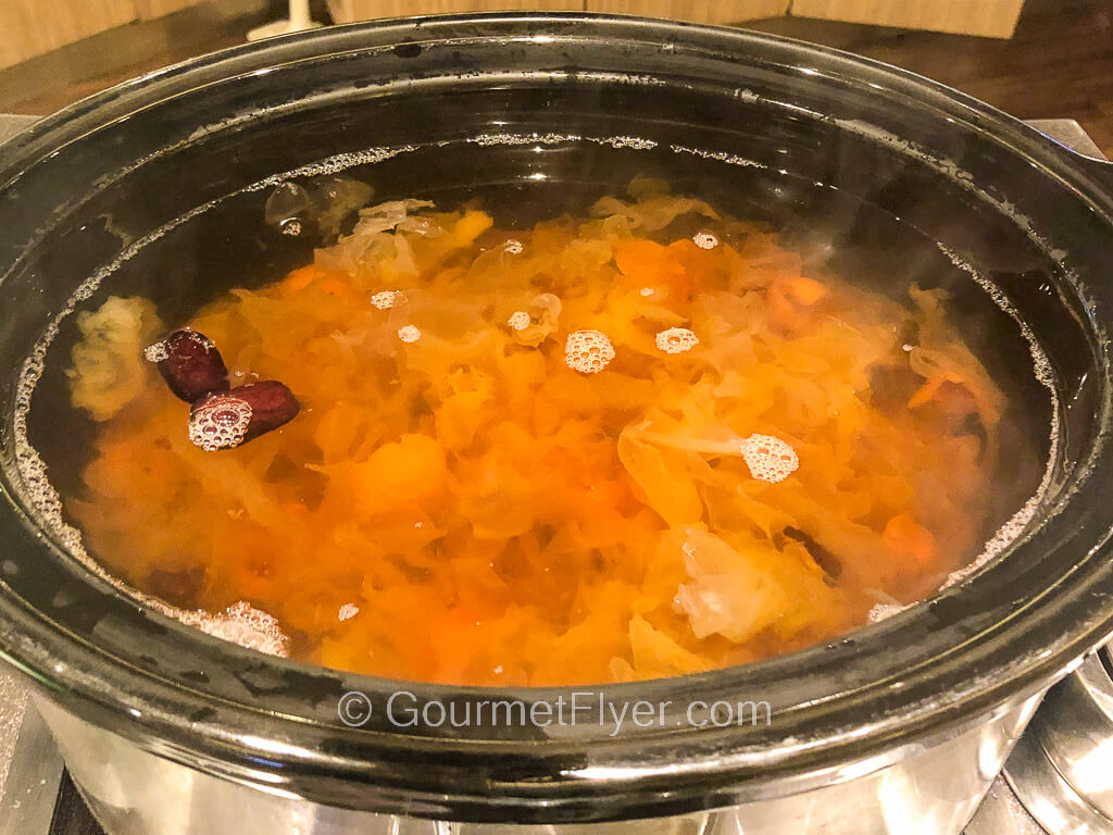 A pot of clear broth with a few red dates floating on its surface.