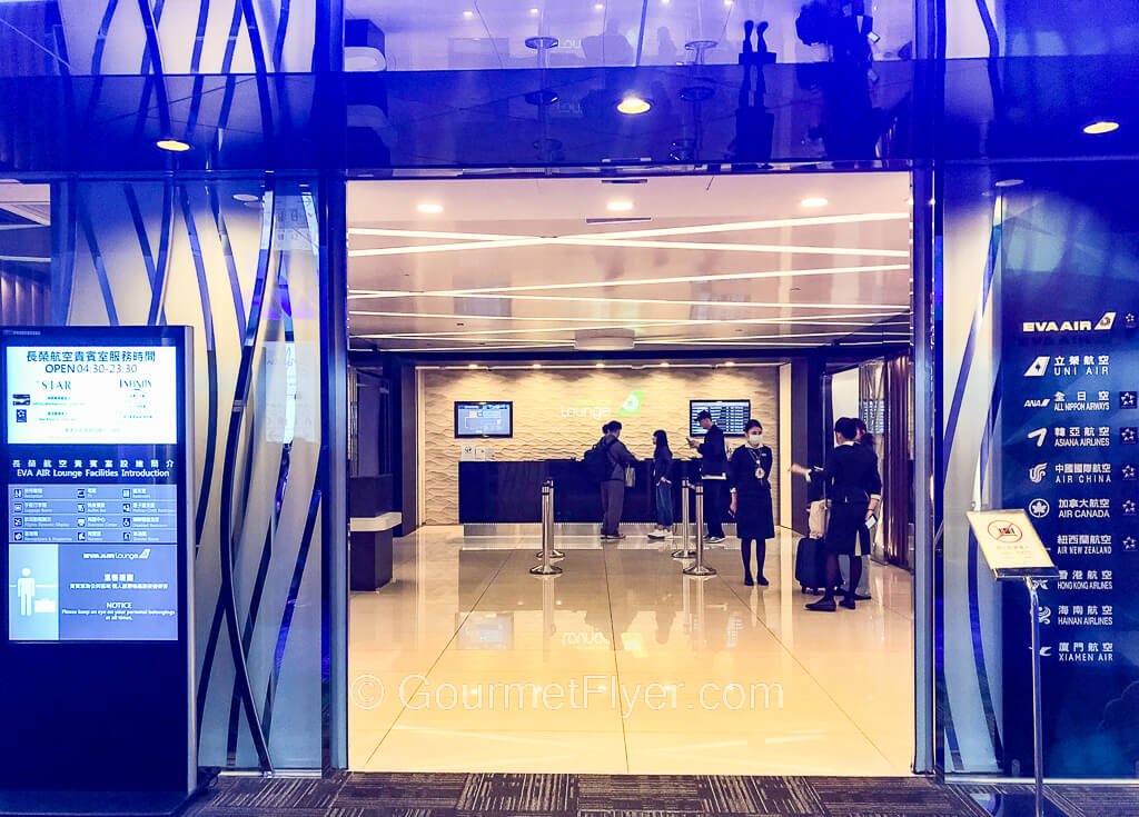 The entrance to an airline lounge is adorned with futuristic looking blue color glass doors that leads to a counter with agents.