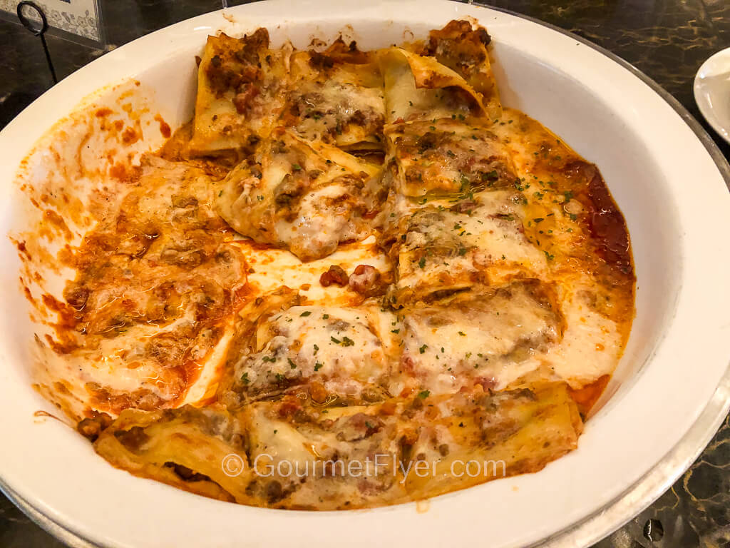 A large round serving bowl is half-filled with precut pieces of lasagne.