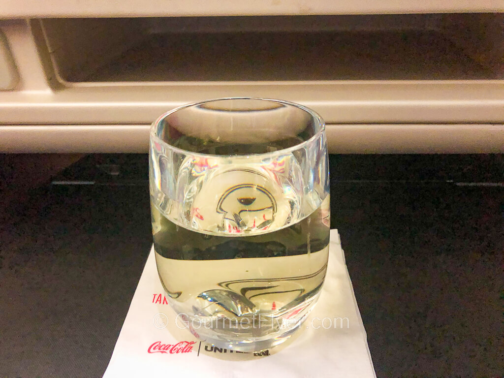 A glass of champagne is placed on a white napkin on top of an airline seat's tray table.