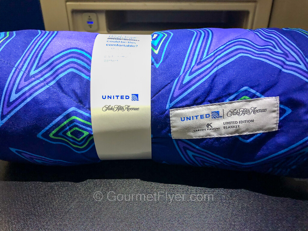 A blue blanket with pattern design is rolled up and placed on the tray table.