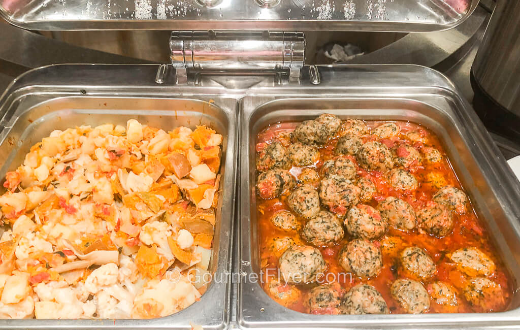 A pair of chaffing dishes contains cauliflower on the left and meatballs in a red sauce in the right.