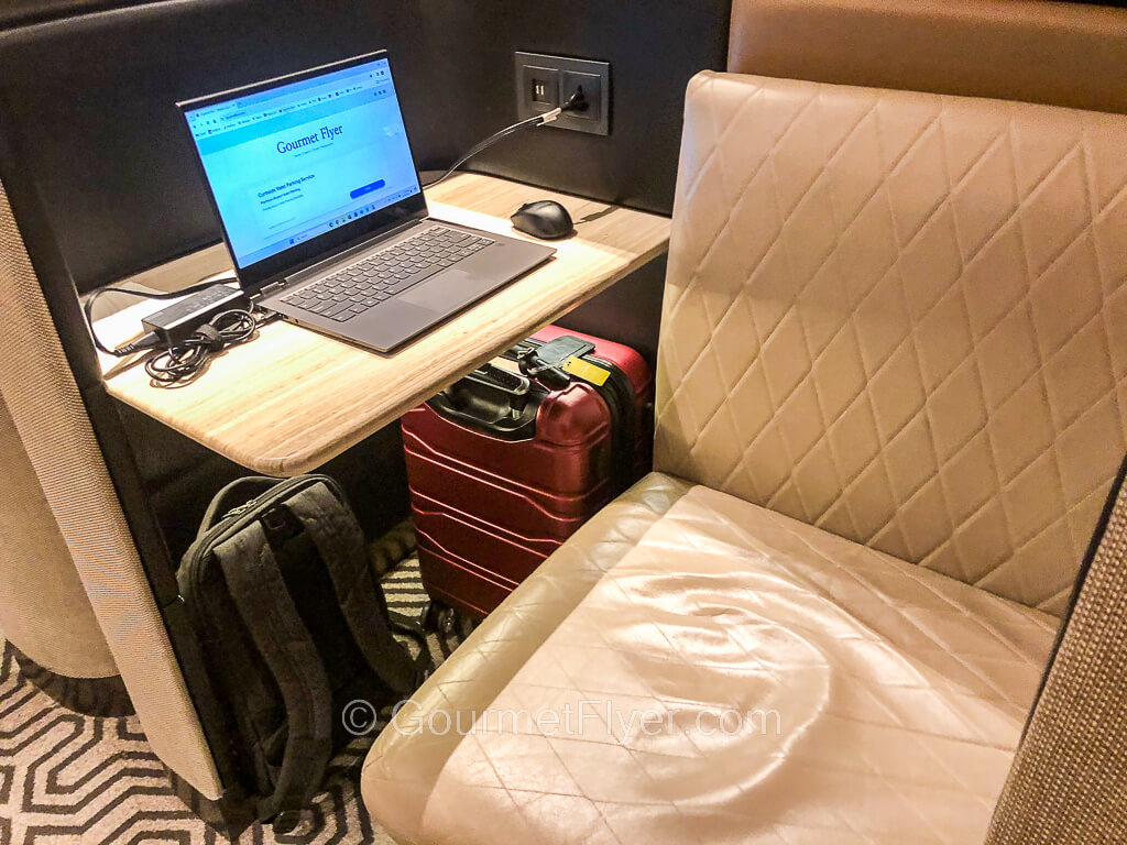 A cubicle has a workspace that is occupied by a laptop computer on top and carryon luggage stored underneath it.