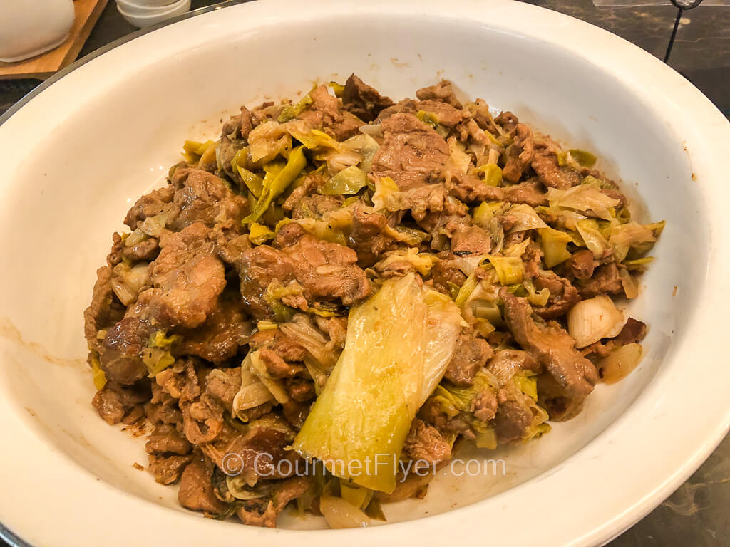A serving platter contains sliced meat stir fried in a brown sauce and garnished with leek.