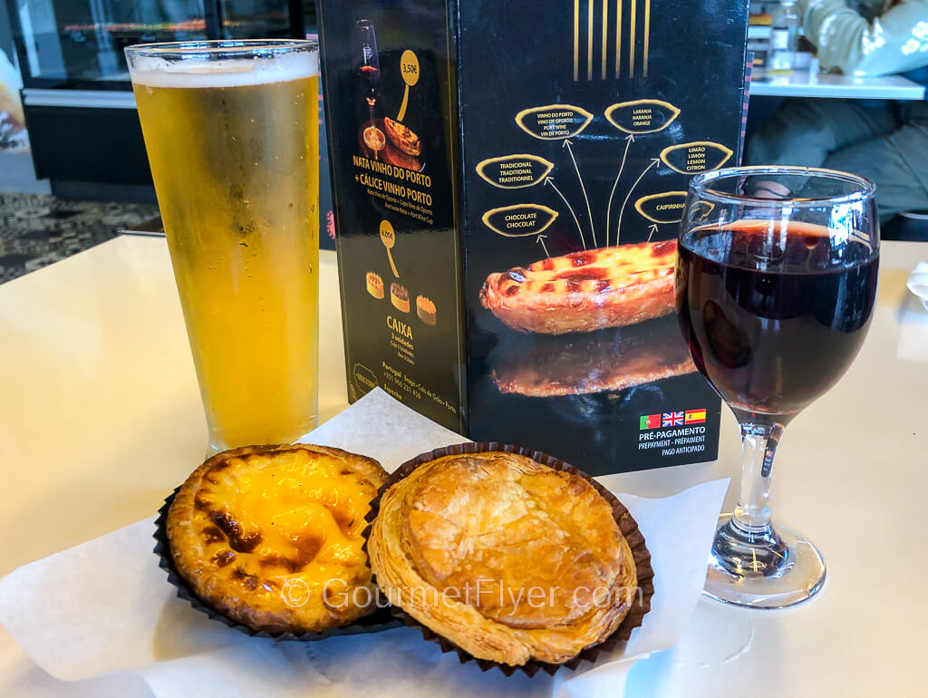 Two custard tarts, one traditional and one savory, are accompanied by a glass of red wine and a glass of beer.