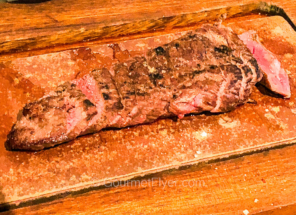 A steak cooked to medium rare is sliced and served on a cutting board.