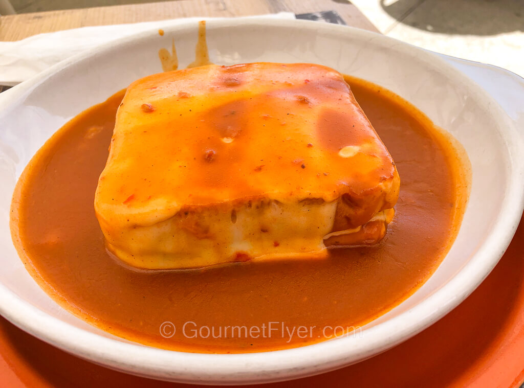 A baked sandwich covered with cheese is served in a saucer with tomato sauce.