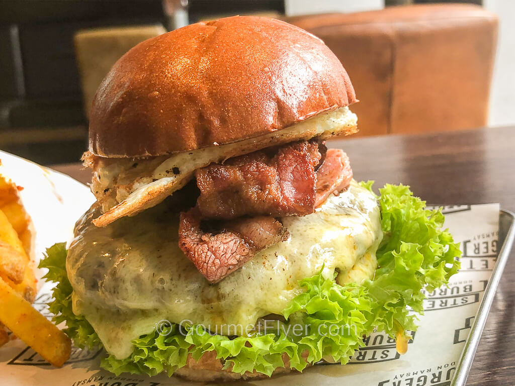 A burger has melted cheese covering the patty and is topped with bacon and a fried egg.
